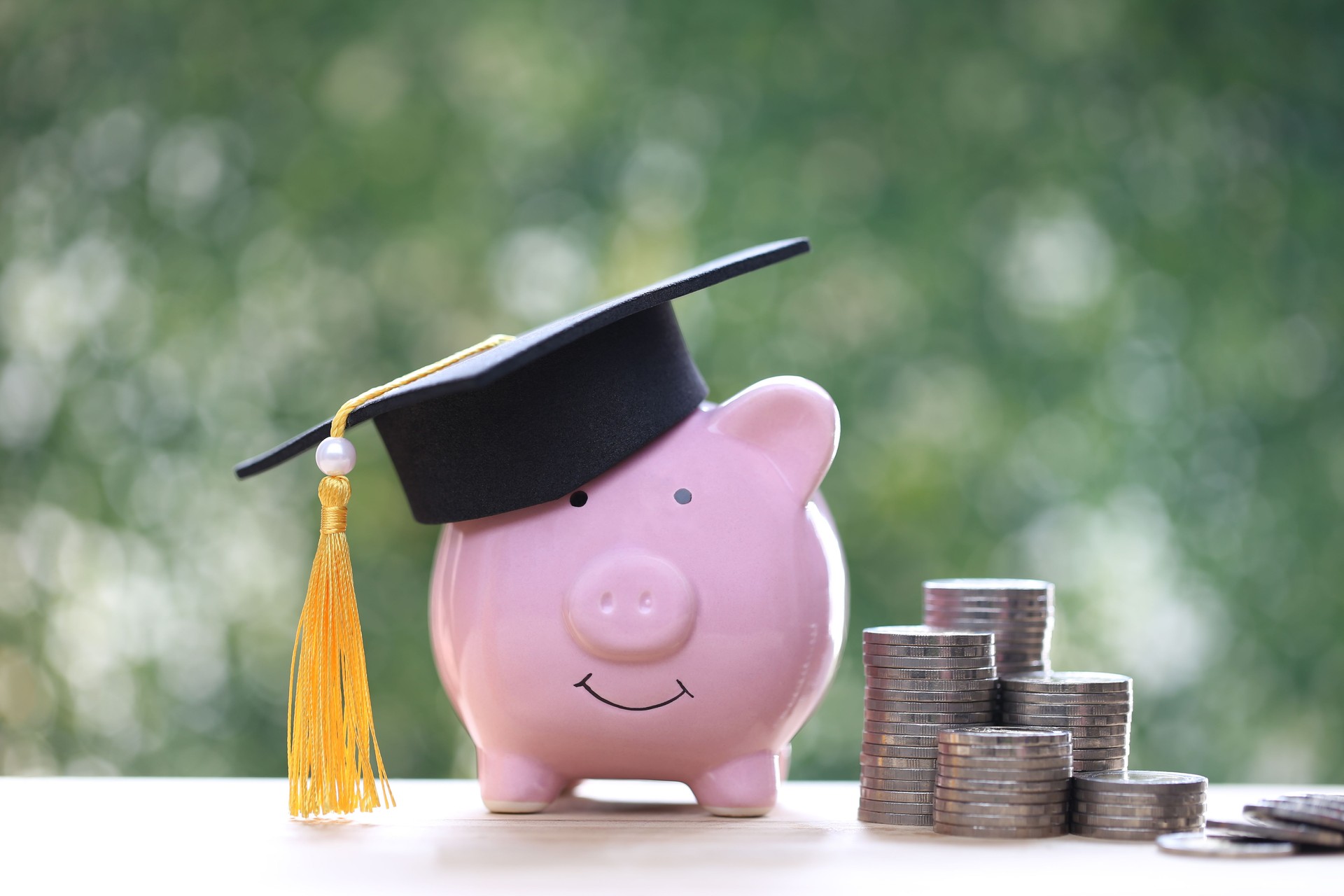 Graduation hat on piggy and stack of coins money on natural green background, Saving money for education concept